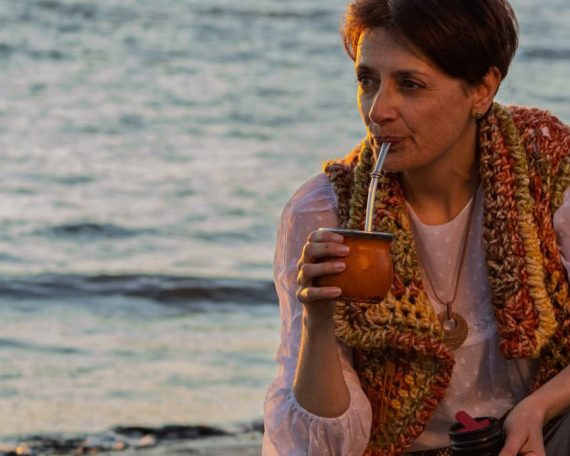 A woman sipping yerba mate while relaxing on a Montevideo beach during sunset.